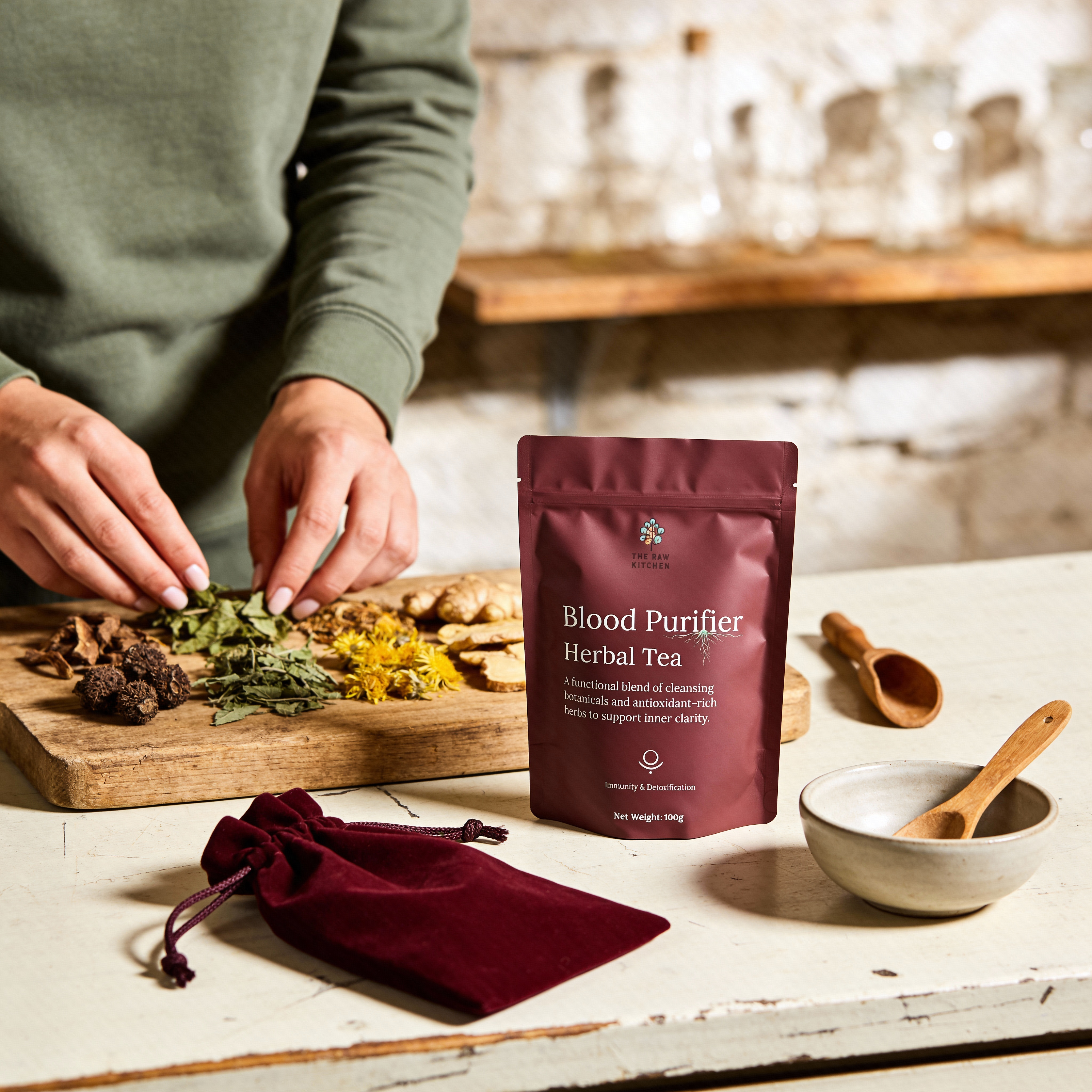 Person preparing herbs on a cutting board with a package of 'Blood Purifier Herbal Tea' on a wooden table.