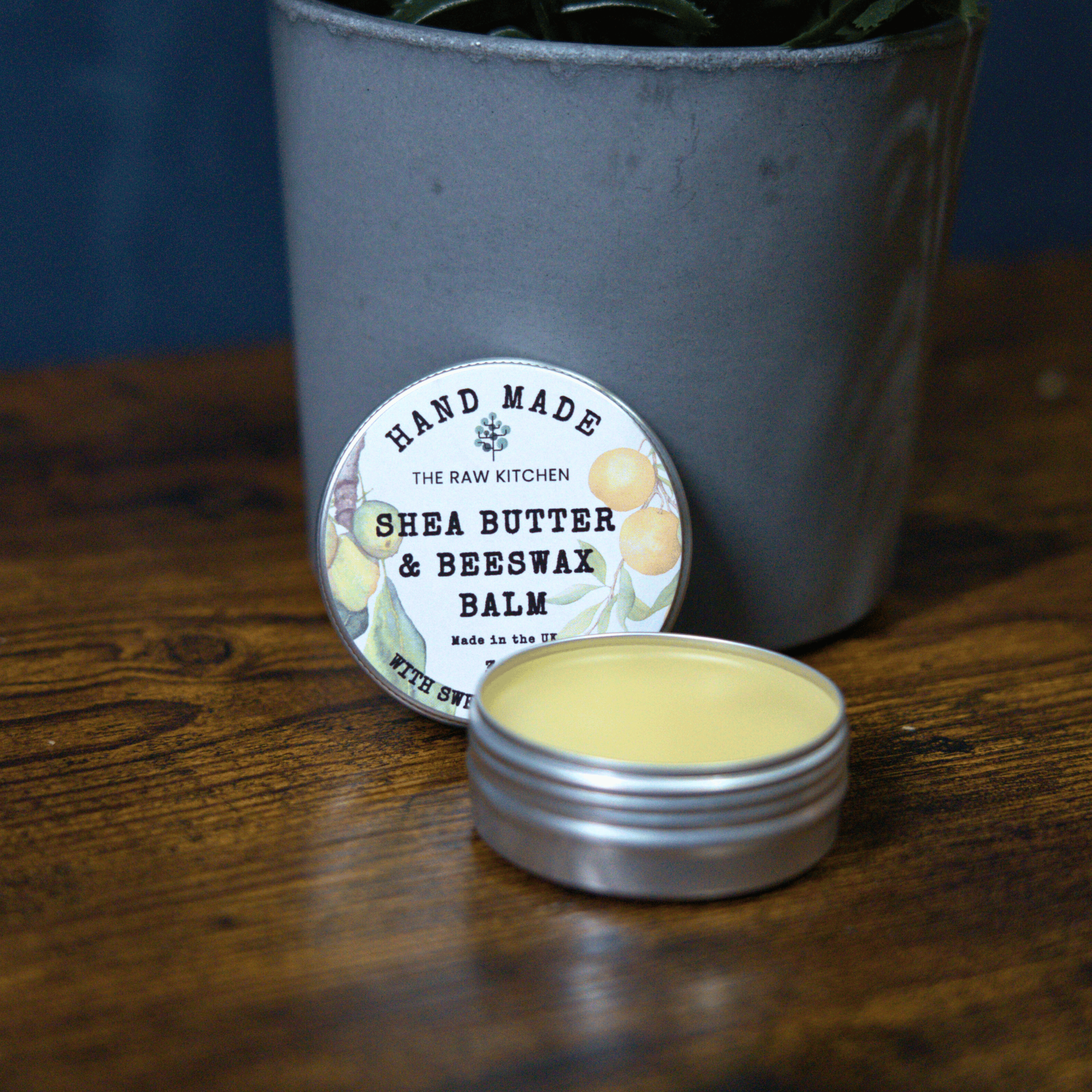 The open tin of handmade Shea Butter & Beeswax Balm, showing the natural texture, on a wooden table - The Raw Kitchen UK.