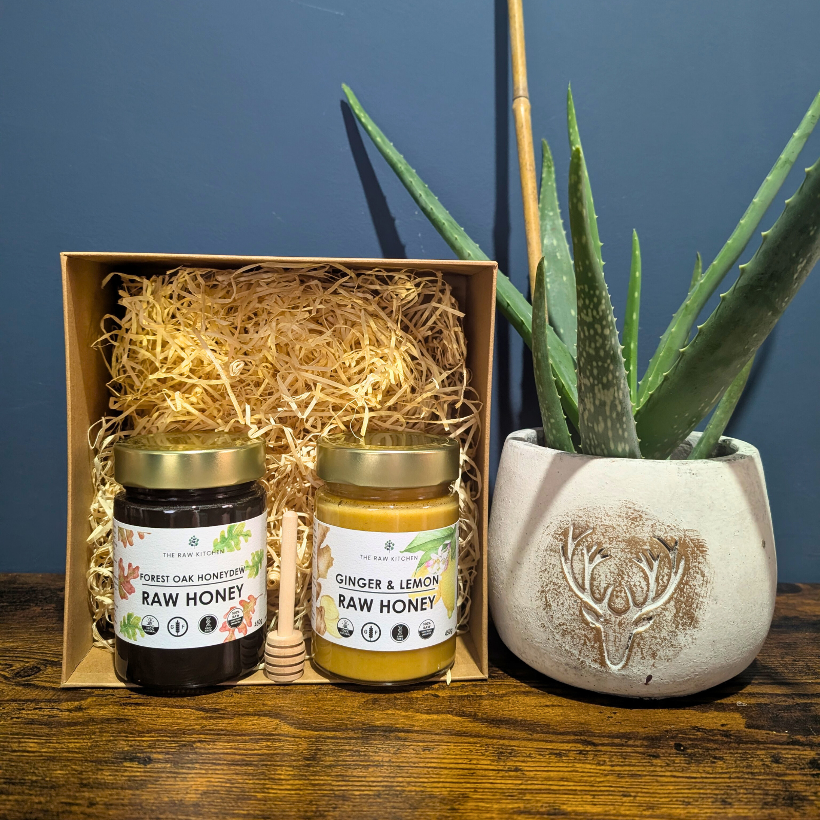 A Raw Honey Gift Box from The Raw Kitchen UK, showing a set of Forest Oak and Ginger & Lemon honeys with a wooden honey dipper.