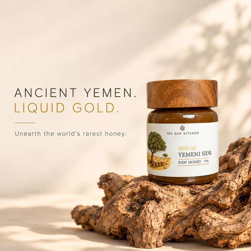 A jar of Royal Yemeni Sidr Raw Honey from The Raw Kitchen sits on a piece of textured driftwood. The background is a warm beige with soft leaf shadows, and the text on the left reads 'ANCIENT YEMEN.