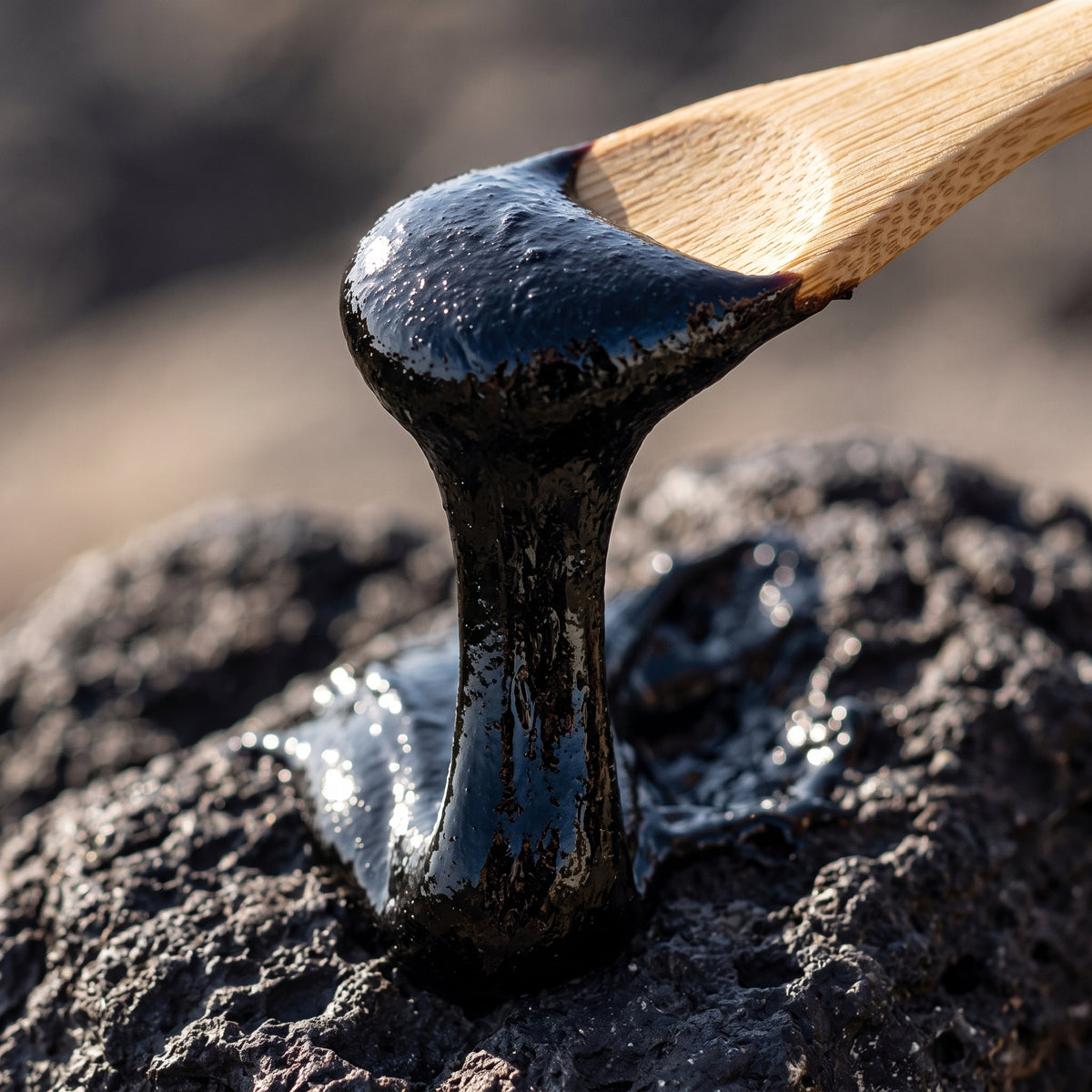 Thick dark shilajit resin on wooden spoon over stone