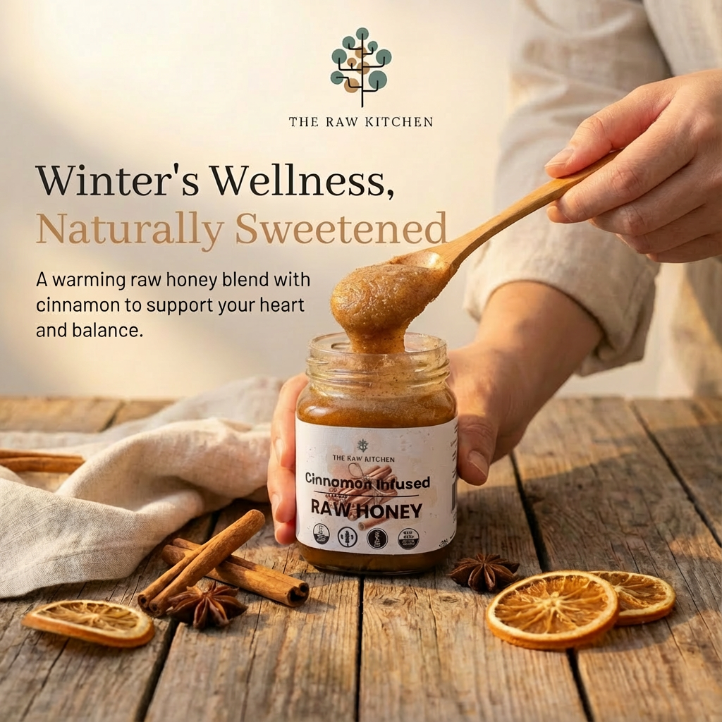 Person holding a jar of 'Cinnamon Infused Raw Honey' with a wooden spoon, surrounded by cinnamon sticks and dried oranges on a wooden surface. Brand 'The Raw Kitchen' is visible.