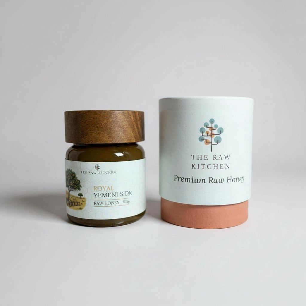 Two containers of honey from The Raw Kitchen on a light gray background