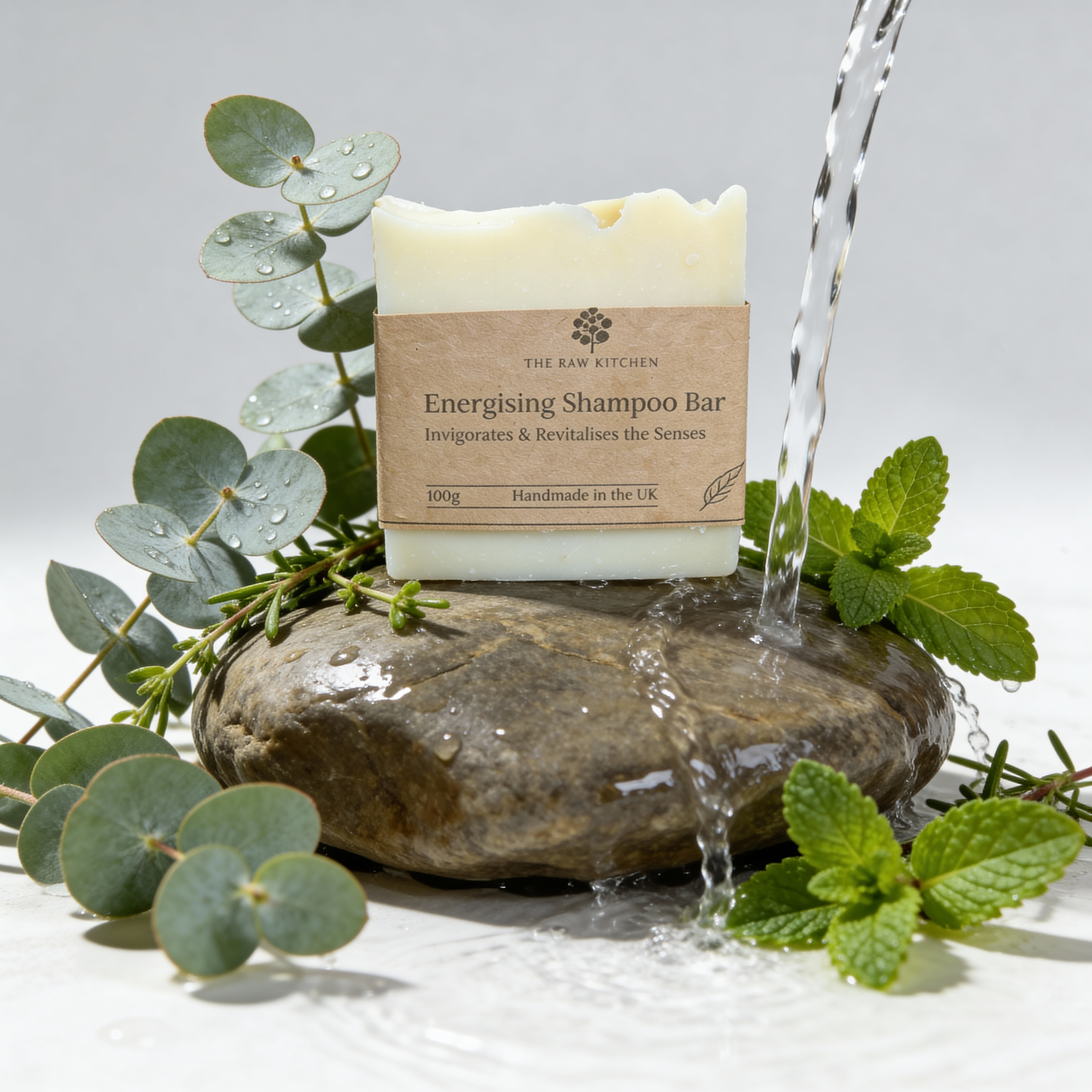 Energising Shampoo Bar from The Raw Kitchen on a stone with water pouring over it, surrounded by greenery.
